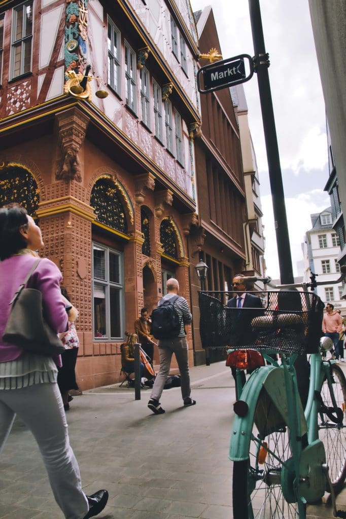 People walking on a sidewalk past as street musician and a bike parked next to a street sign