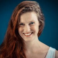 Smiling woman with long side swept hair in front of a blue backdrop