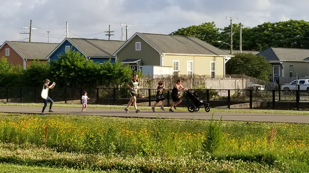 People walking and running with a stroller on the Lafitte Greenway path in New Orleans in front of houses