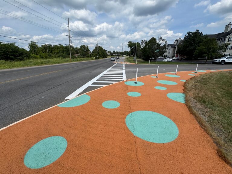 a crosswalk at an intersection with a painted bike and walking path and delineators