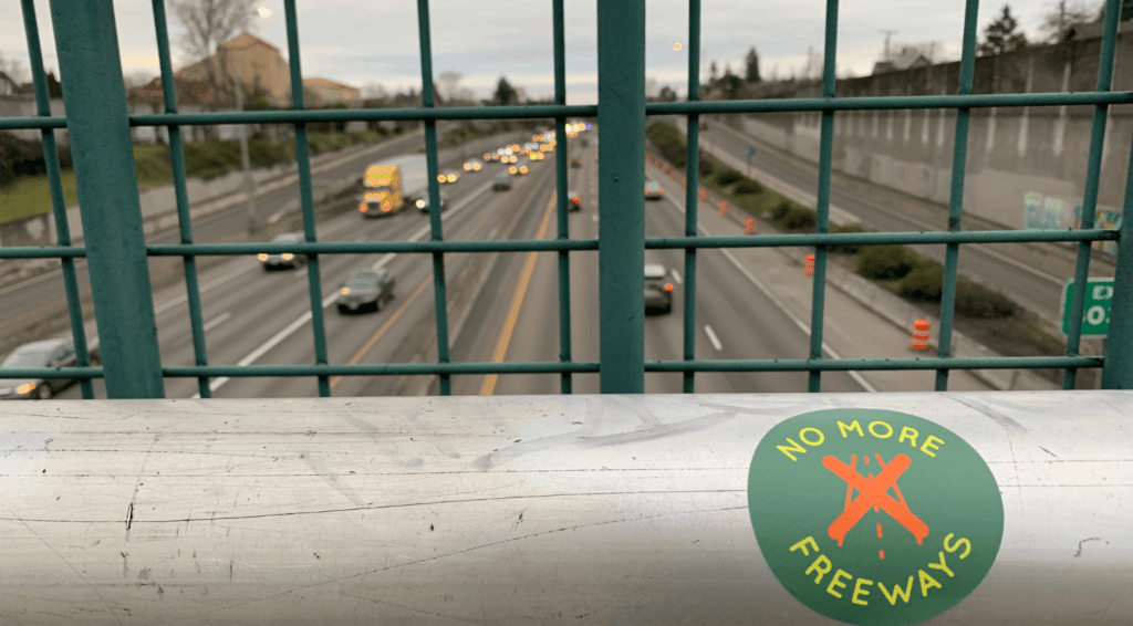 an overhead view of a highway from a bridge with a sticker reading no more freeways on a railing
