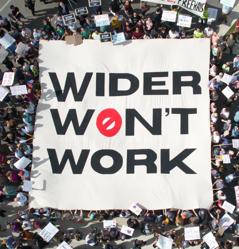 Aerial view of a large crowd surrounding a giant banner reading Wider Won't Work